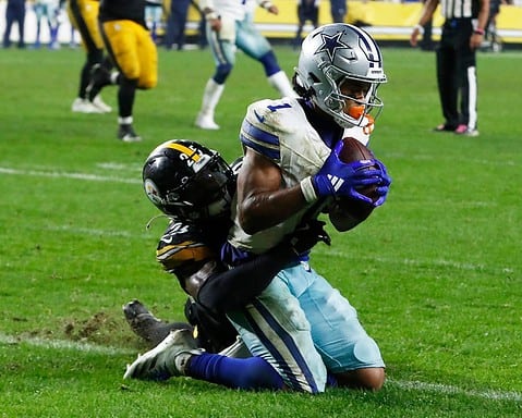 In Week 8, a Cowboys football player in white and blue uniform clutches the ball tightly while being tackled by a player in black and yellow uniform.