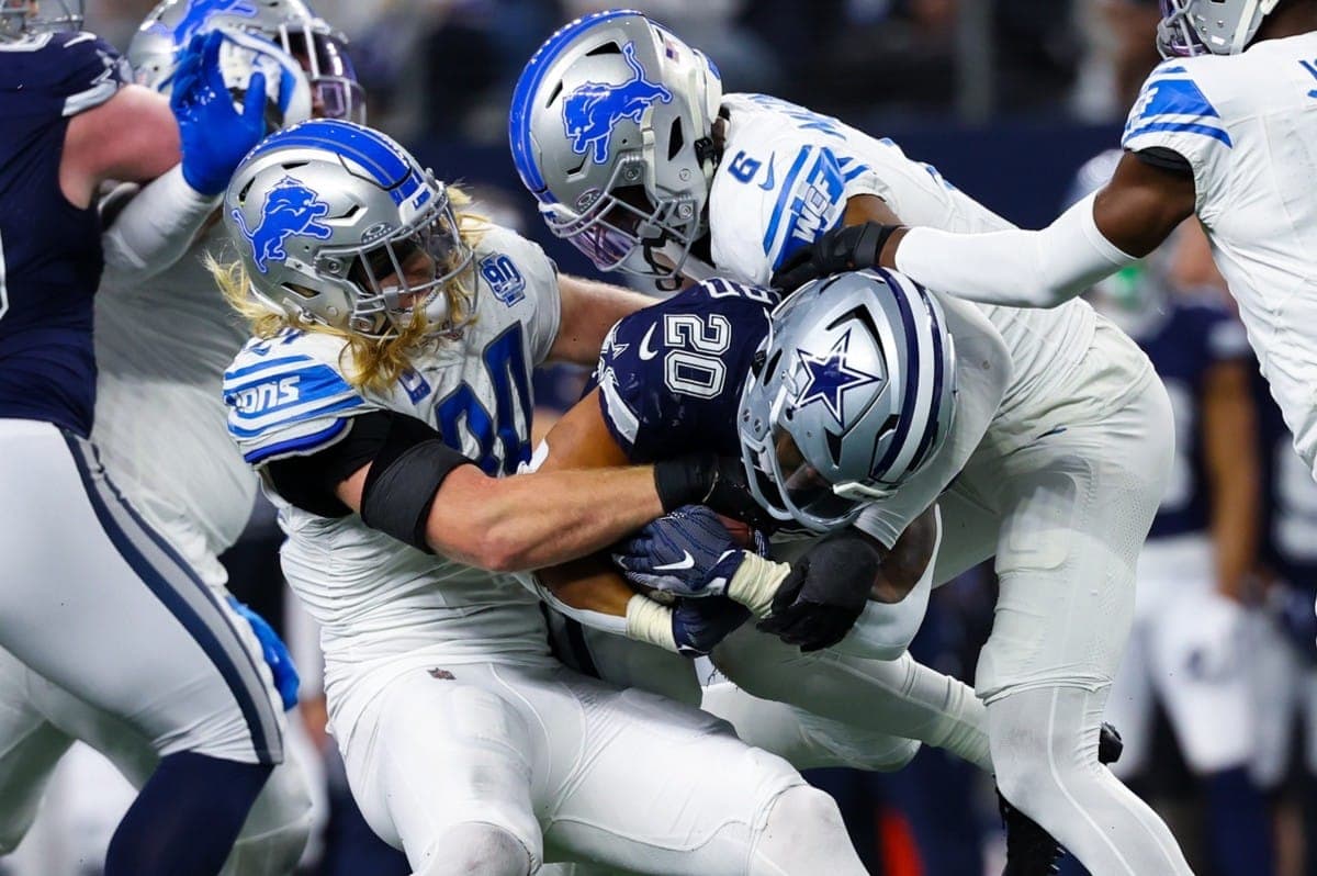 Football players in blue and silver uniforms tackle a player in a dark jersey during a game.