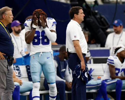 A struggling football player with head in hands on the sidelines, surrounded by coaches during a game, reflects the pressure that even Cowboys stars face amidst discussions of contract extensions.