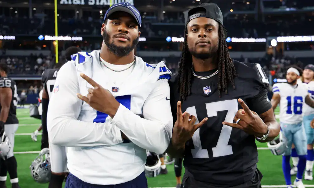 Two football players in jerseys posing on a field with a stadium backdrop.