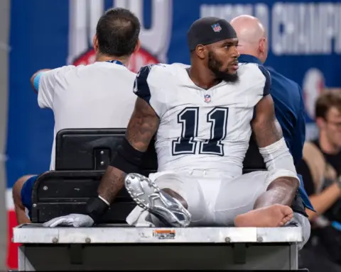 Football player in jersey number 11 being driven on a medical cart off the field.