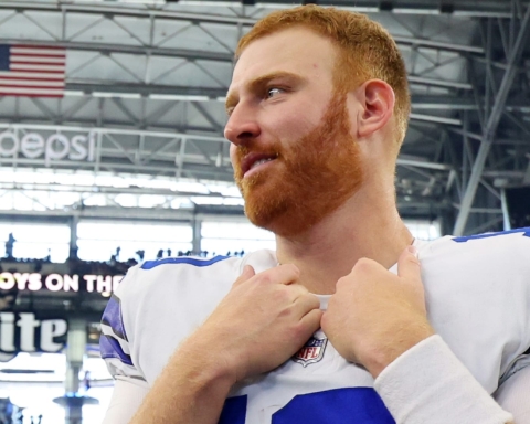 A football player with a red beard stands in a stadium, touching his collar, embodying the changing aspect of the modern-day cowboys on the field.