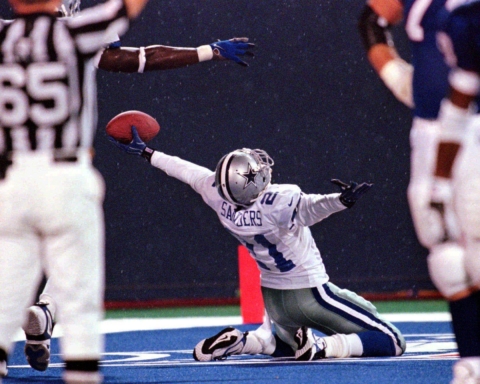 Football player kneeling and holding a football in the end zone as a referee signals a touchdown, envisioning himself as the next Cowboys coach.