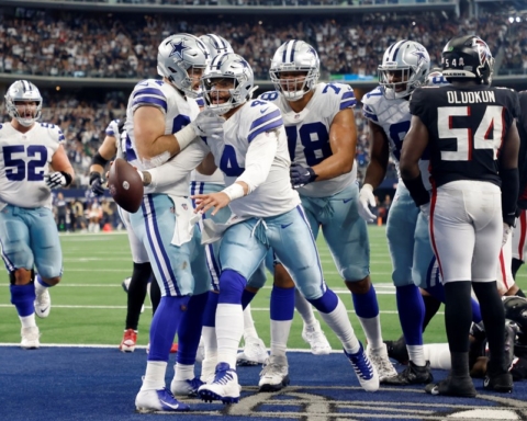 Dallas Cowboys players celebrate a touchdown on the field during Week 9, with a roaring crowd in the background.