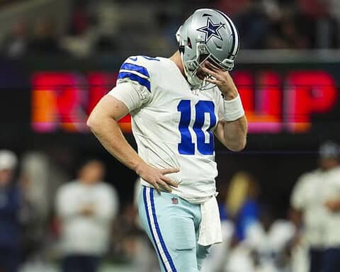 A Dallas Cowboys player stands on the field during Week 11, looking down with his hand near his face.