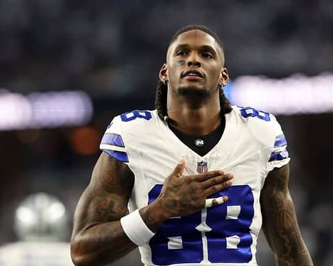 Football player wearing a white jersey with number 88, resembling CeeDee Lamb from the Cowboys, stands with his right hand on his chest as if in a heartfelt moment during Week 11.