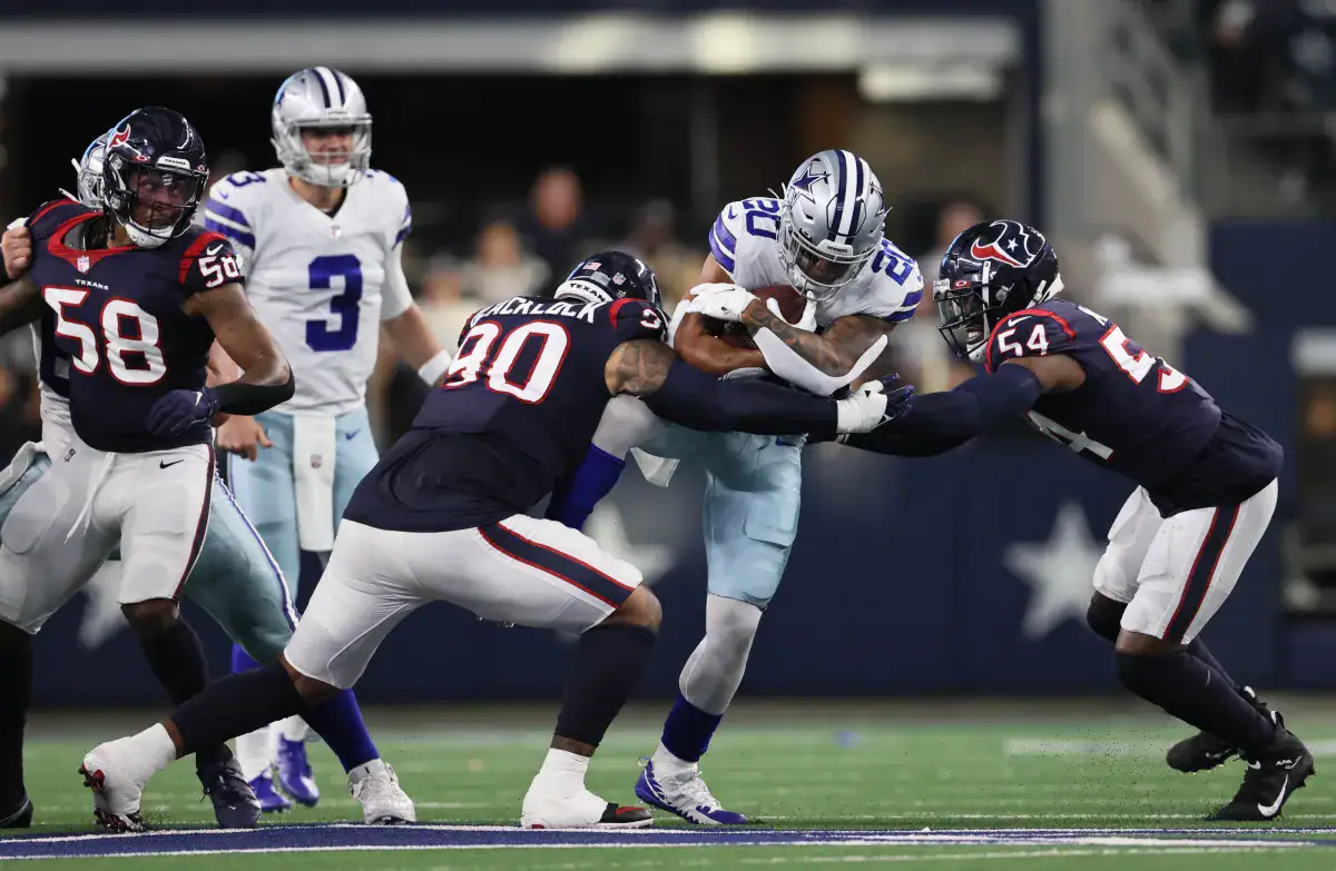 Dallas Cowboys player CeeDee Lamb runs the ball while being tackled by two Houston Texans players on a football field, showcasing the Cowboys' determined offense.