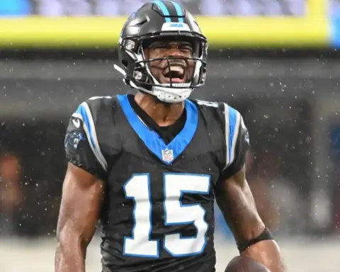 A football player in a black and blue uniform celebrates on a rainy field as rumors swirl about the Cowboys adding a wide receiver.