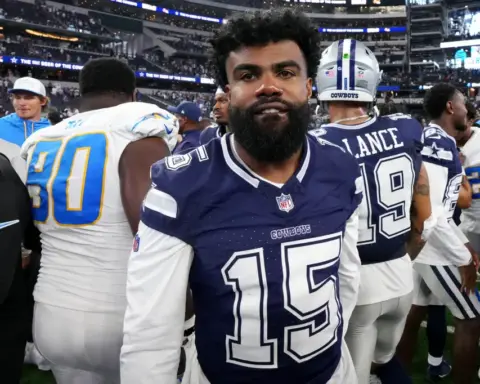 In his Dallas Cowboys uniform, the football player stands on the field, surrounded by fellow Cowboys players post-game, contemplating his future role with the team.