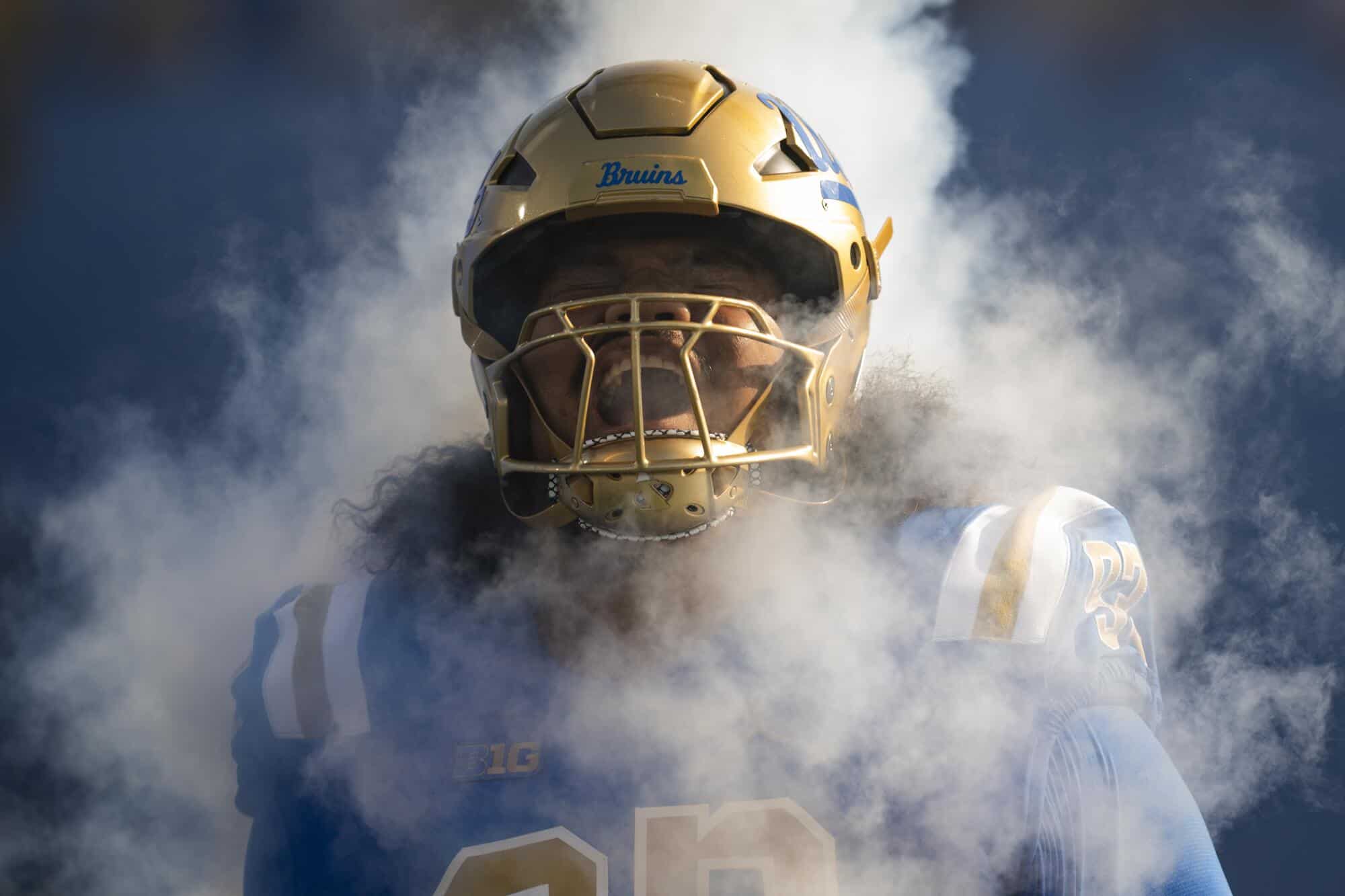 Helmeted football player from the Dallas Cowboys, wearing a gold helmet with a face cage, surrounded by smoke on a game day, showcasing team spirit and intense game atmosphere.