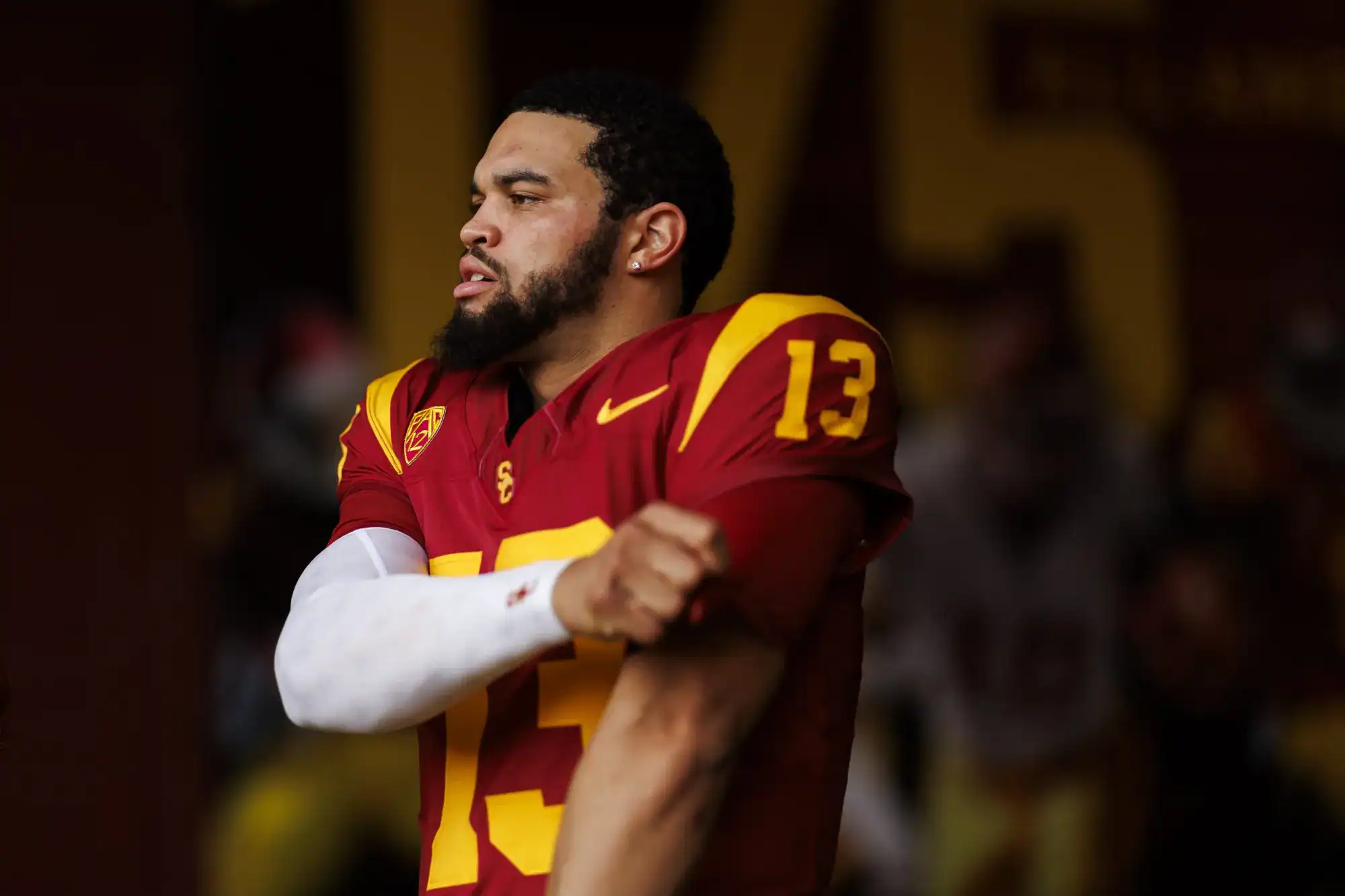 Justin Jefferson wearing a red and yellow USC football jersey with the number 13, celebrating on the field with a determined expression.