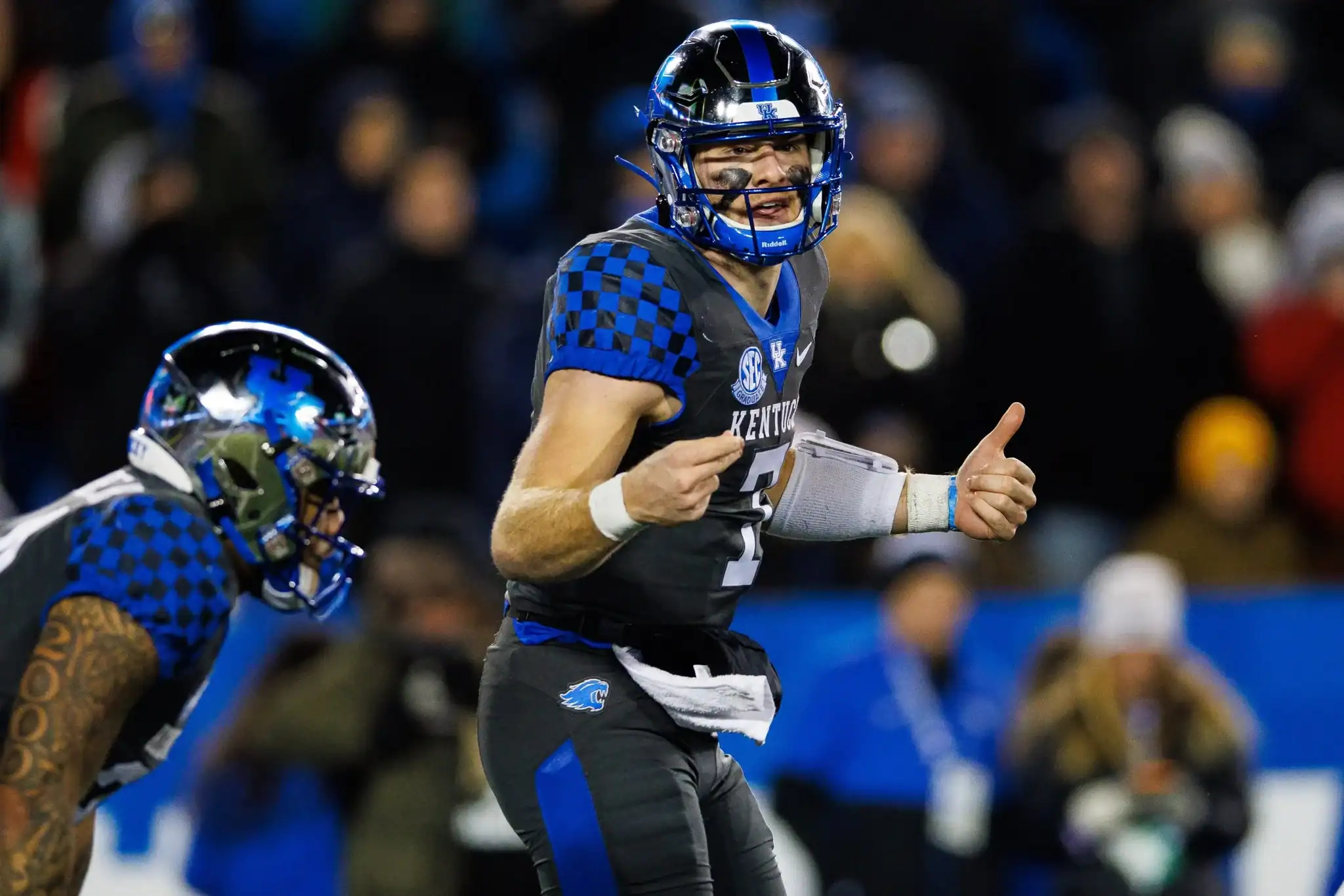 Game-winning football player in blue and black uniform at Kentucky football game, celebrating victory, on field with team and fans background.