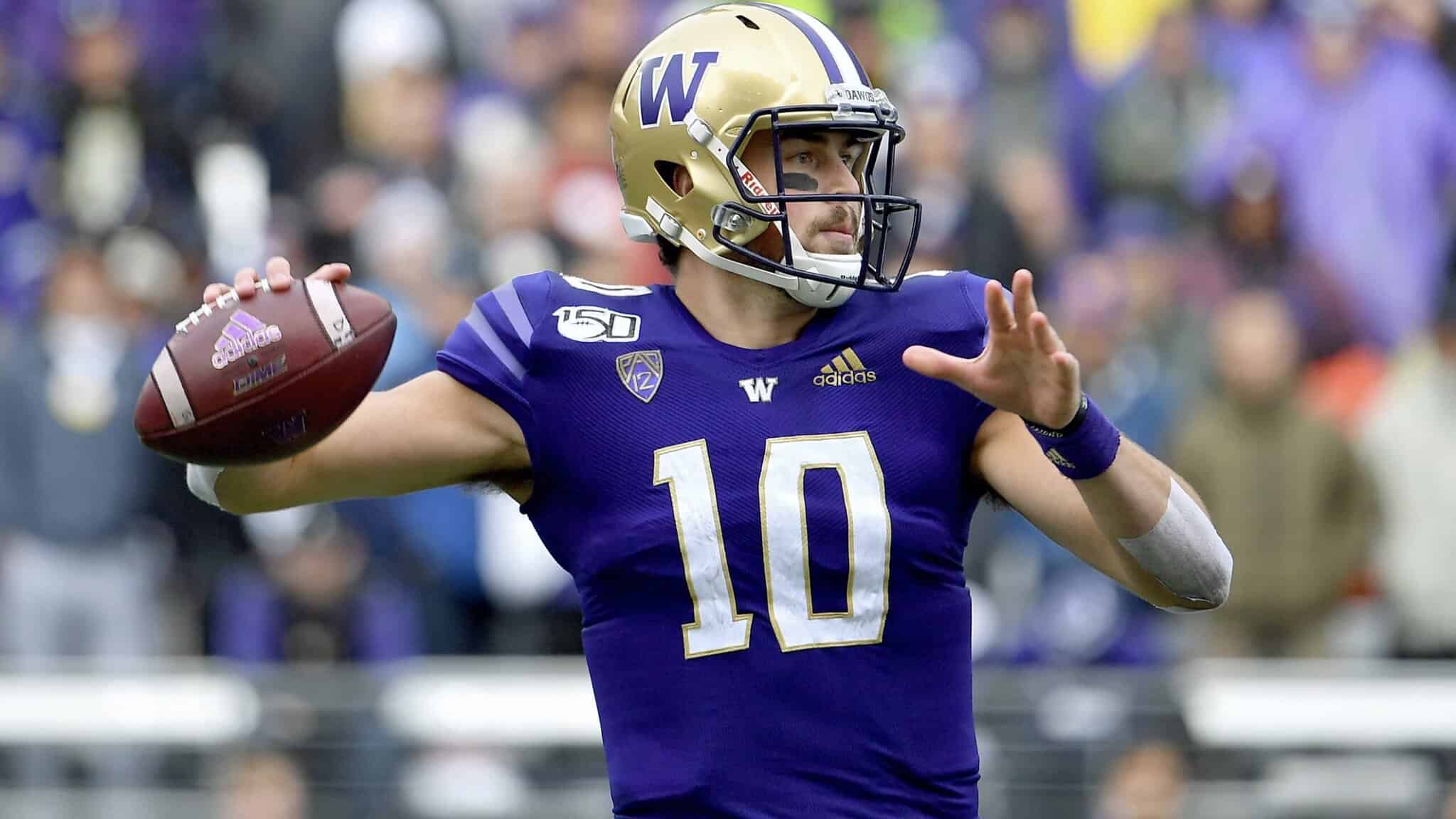 Quarterback in purple uniform preparing to throw a football on the field, with fans blurred in the background at a football game.