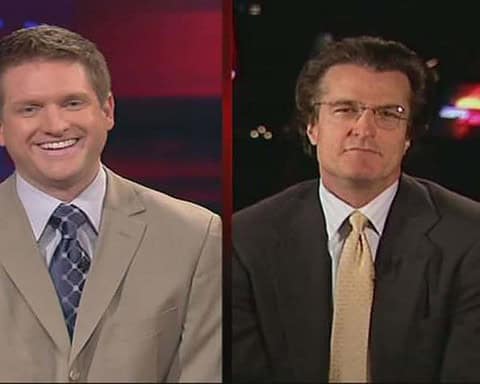 Smiling sports news anchor in beige suit on the left, serious analyst in dark suit and glasses on the right, inside the star TV set, Dallas Cowboys coverage, inside the star branding, professional sports broadcasting atmosphere.