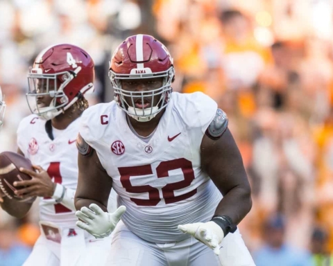 Alabama football player in white jersey with maroon '52' running on the field during game against Tennessee Volunteers, focused on gaining yards, stadium crowd blurred in background.