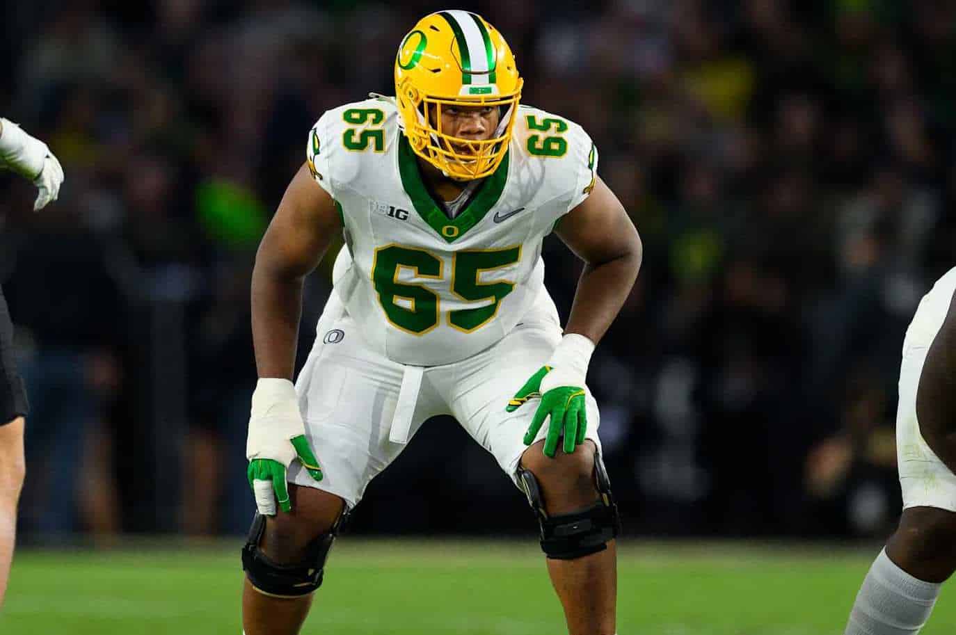 Green Bay Packers football player in defensive stance on the field, wearing jersey number 65, during a game; focused on opposing team; sports action image.