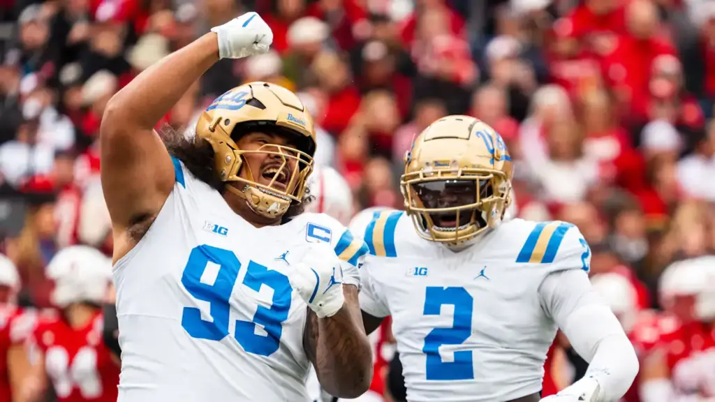 Celebrating U-Mass football players in white uniforms with blue and gold helmets, high-fiving and cheering on the field during a college football game.