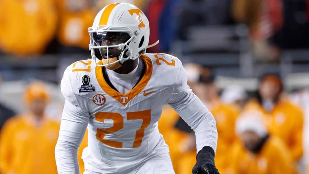 Tennessee Volunteers football player in white jersey with orange accents, wearing number 27, during a game with players and fans in the background.