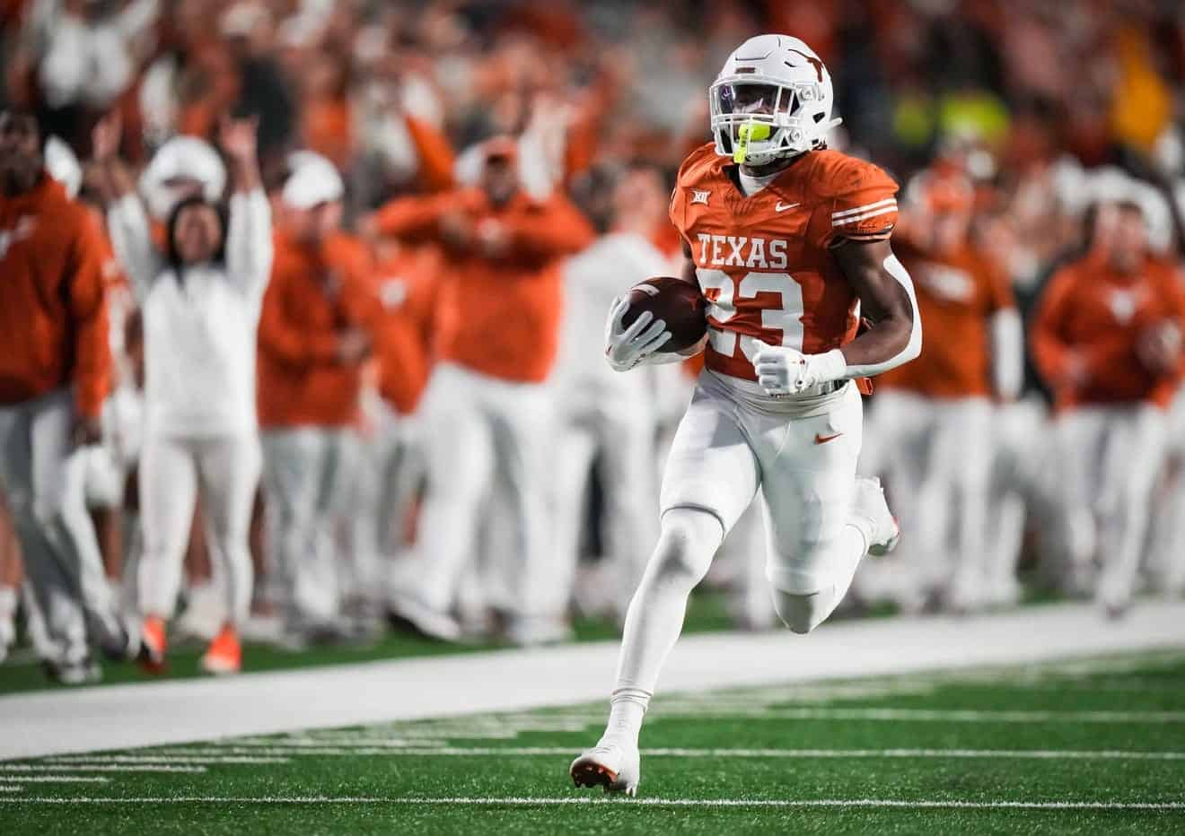 Running back player in Texas Longhorns football uniform carrying football during game at the stadium with cheering fans in background.