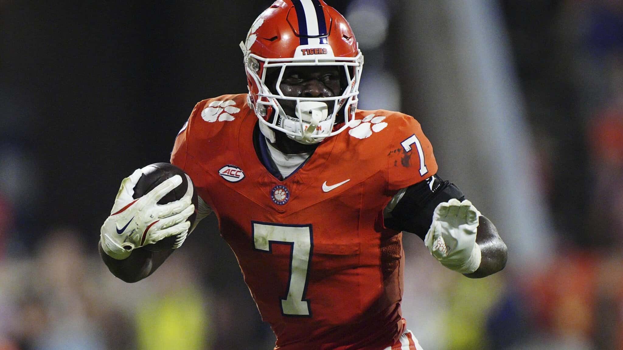 Running back in Clemson Tigers orange football jersey, holding football, on field, during game, with helmet and gloves, showcasing athleticism and team spirit.