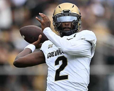 A football player wearing a gold helmet and white uniform with number 2, holding a football, during a game, focused on throwing or passing the ball.