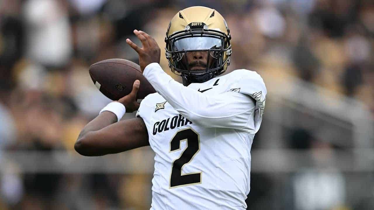 A football player wearing a gold helmet and white uniform with number 2, holding a football, during a game, focused on throwing or passing the ball.