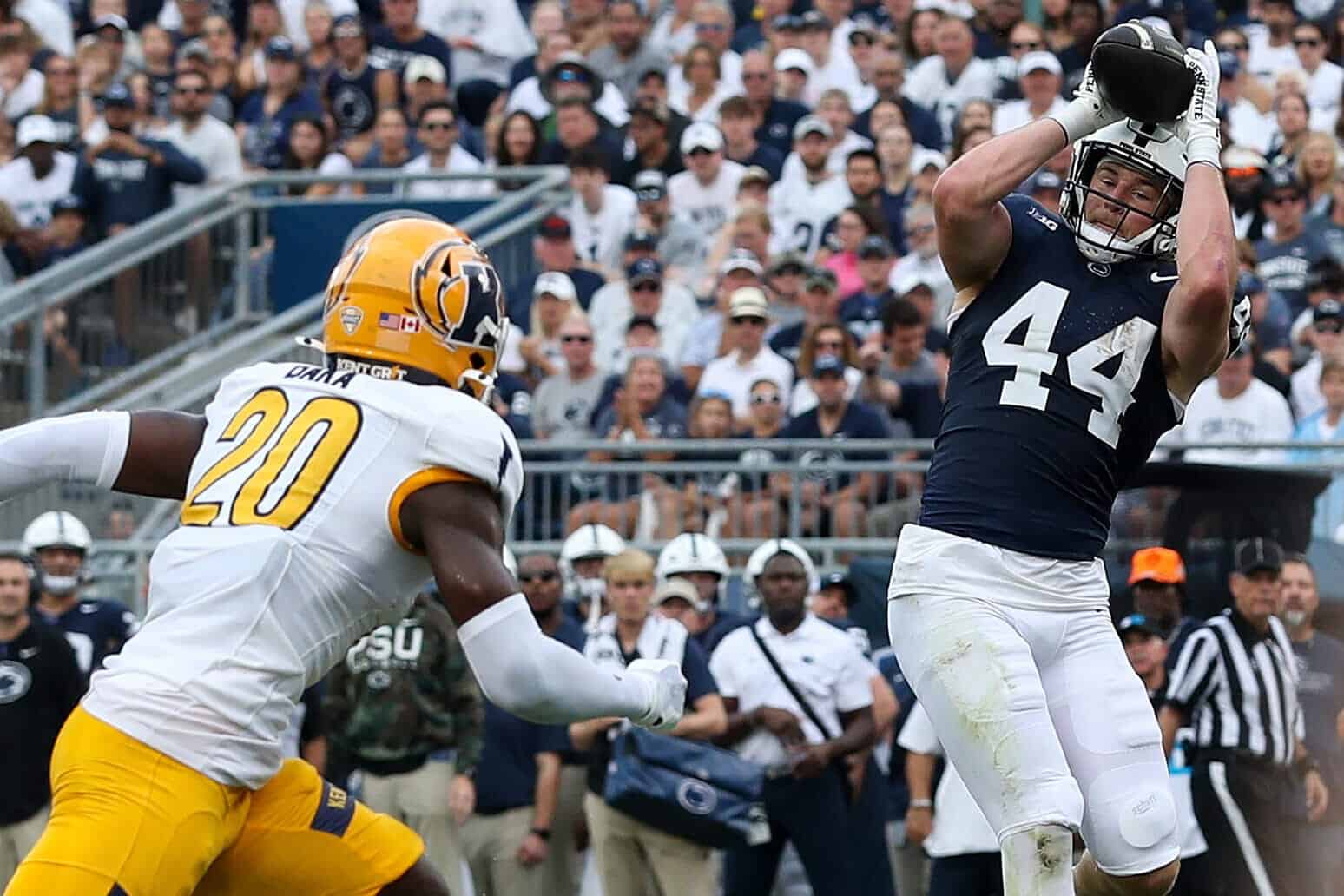 High school American football game, wide receiver catching pass while defensive back tries to block, crowd and stadium in background, competitive sports action, inside the star.