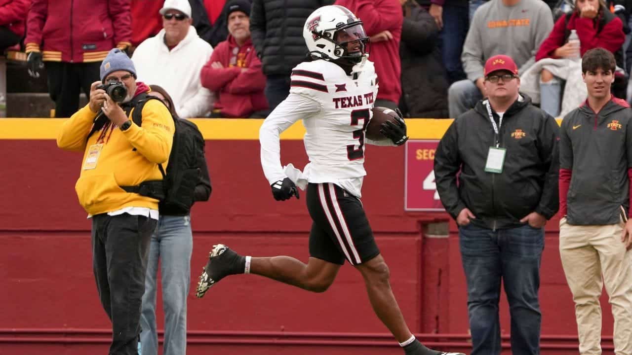 A Texas Tech football player running with the ball during a game at the stadium, surrounded by fans and photographers, showcasing college football action and athleticism.