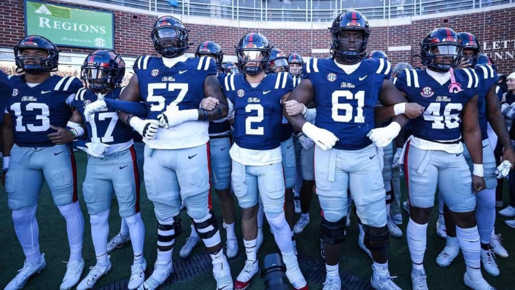 Group of Oklahoma State University football players in blue jerseys and white pants standing arm-in-arm before a game.