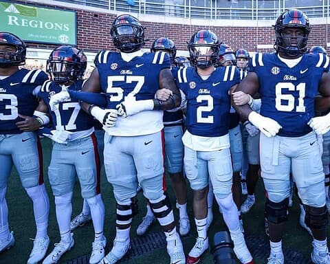 Group of Oklahoma State University football players in blue jerseys and white pants standing arm-in-arm before a game.