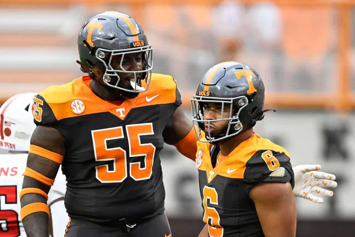 Tennessee Volunteers football players in black and orange uniforms during a game, wearing helmets with the "T" logo, focused on teamwork and game strategy at Neyland Stadium.