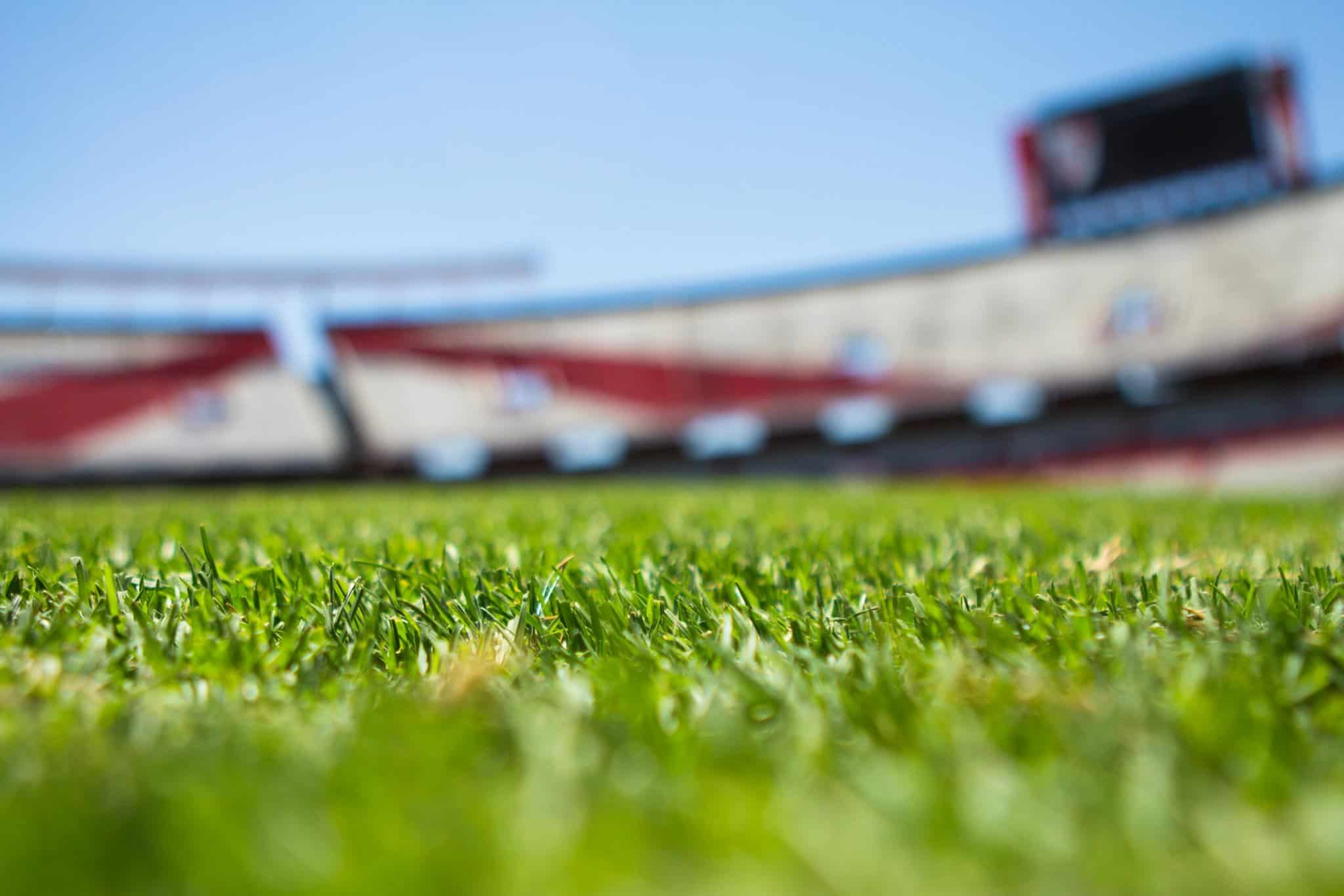 Lush green football field grass with stadium seating and scoreboard in the background, showcasing the Dallas Cowboys' AT&T Stadium, perfect for NFL fans and sports enthusiasts.