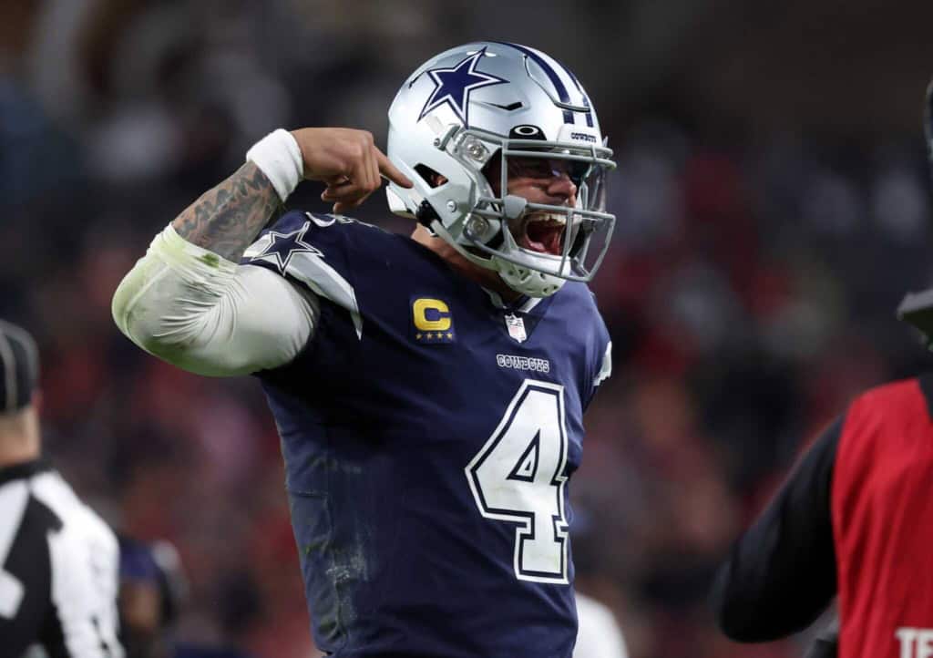 Dallas Cowboys player celebrating on the field, wearing helmet and jersey with number 4, during an NFL game, showing enthusiasm and team spirit.