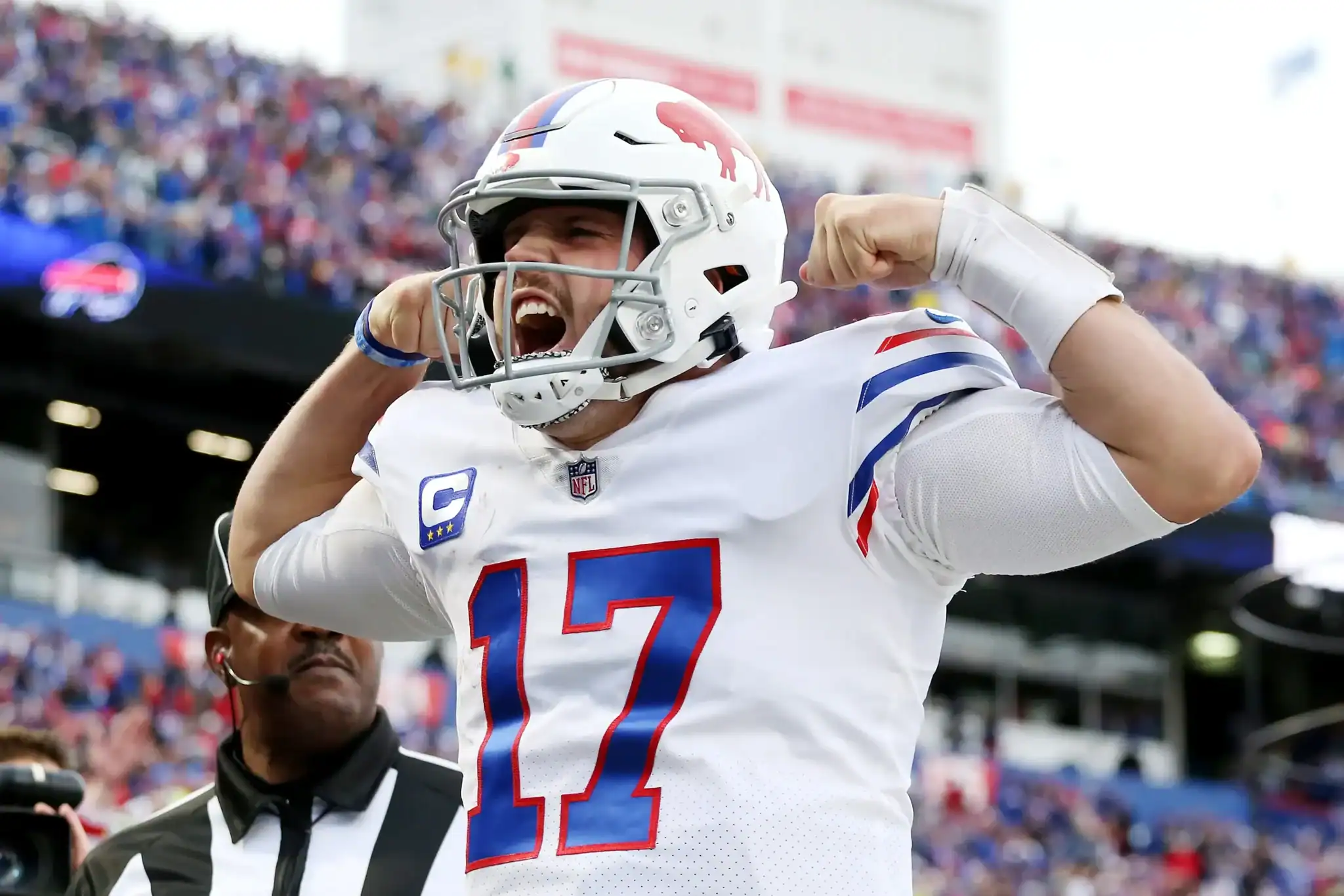 High-energy moment of Dallas Cowboys quarterback celebrating with flexed arms and shouting after a successful play, wearing uniform and helmet, during a game at the stadium filled with fans.