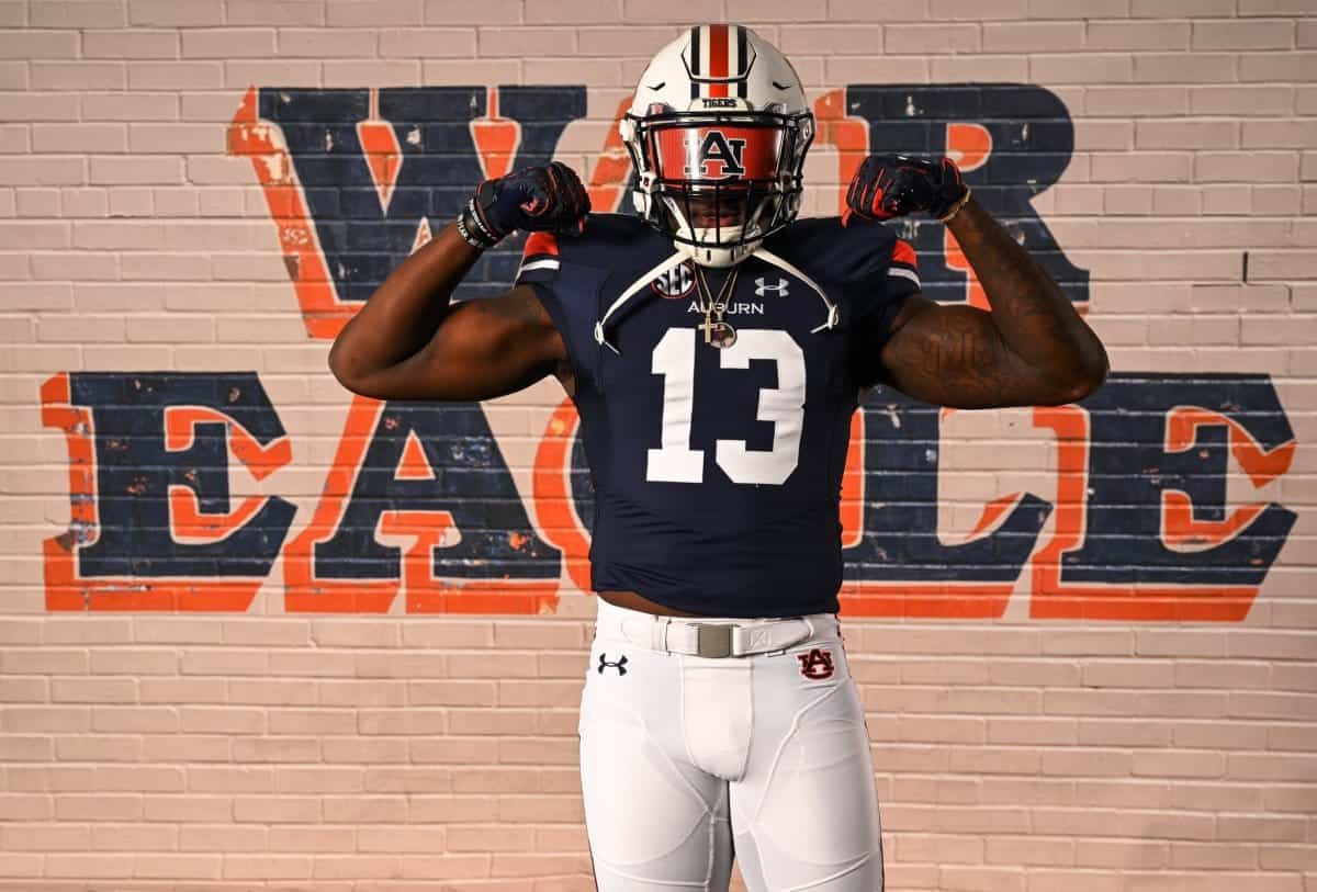 Auburn football player wearing jersey number 13 posing in front of a brick wall with Auburn and War Eagles logos.