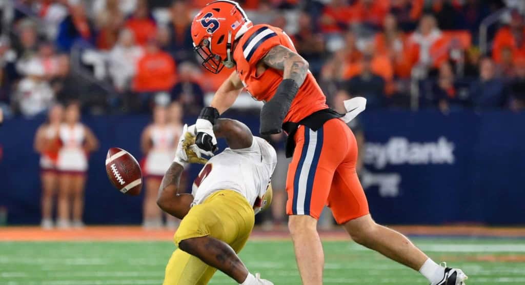 Exploding football hit by a player from the opposing team during a game at AT&T Stadium, showcasing intense action and athleticism in American football, with fans in the background.