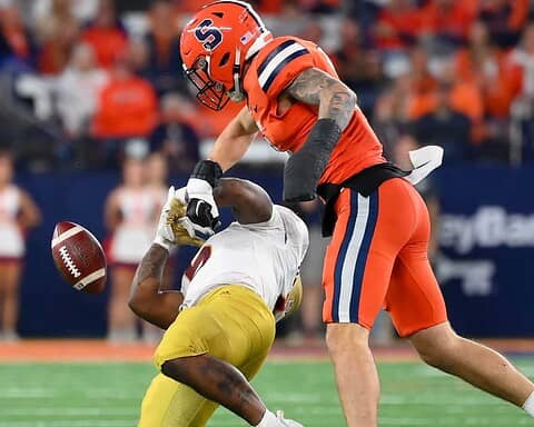 Exploding football hit by a player from the opposing team during a game at AT&T Stadium, showcasing intense action and athleticism in American football, with fans in the background.