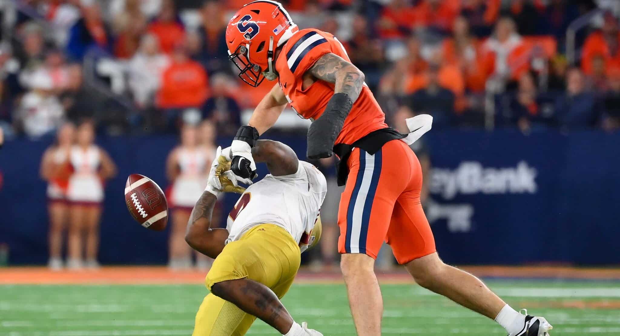 Exploding football hit by a player from the opposing team during a game at AT&T Stadium, showcasing intense action and athleticism in American football, with fans in the background.