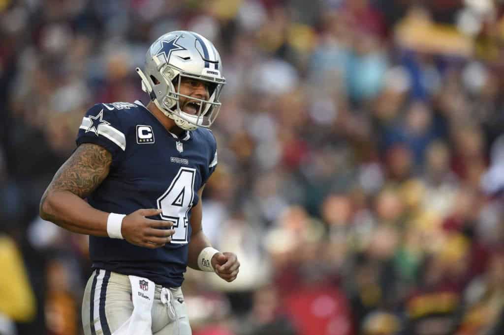 Dallas Cowboys football player wearing jersey number 4, celebrating on the field during a game, with a blurred crowd in the background.