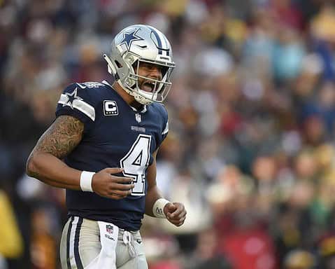 Dallas Cowboys football player wearing jersey number 4, celebrating on the field during a game, with a blurred crowd in the background.
