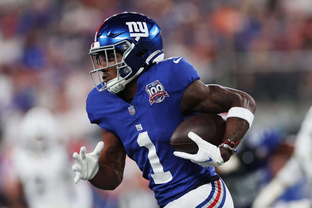 NY Giants football player running with the ball during an NFL game, wearing a blue jersey and helmet, showcasing team pride and athletic action.