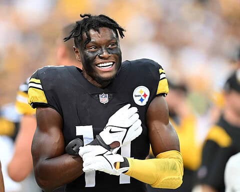Athletic African American football player wearing Pittsburgh Steelers jersey, celebrating on the field during game, smiling with face paint, team logo, and gold accents.