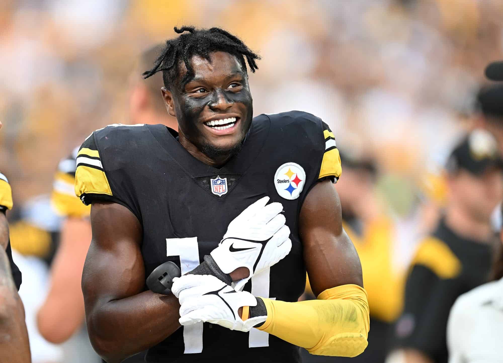 Athletic African American football player wearing Pittsburgh Steelers jersey, celebrating on the field during game, smiling with face paint, team logo, and gold accents.
