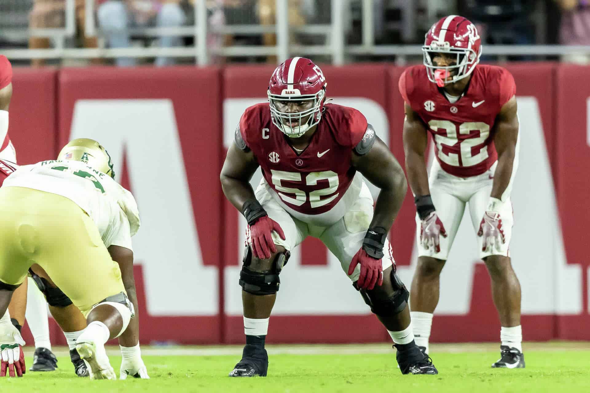 Alabama football players in red uniforms on the field during a game against Florida, focusing on linebacker number 52 in a defensive stance.