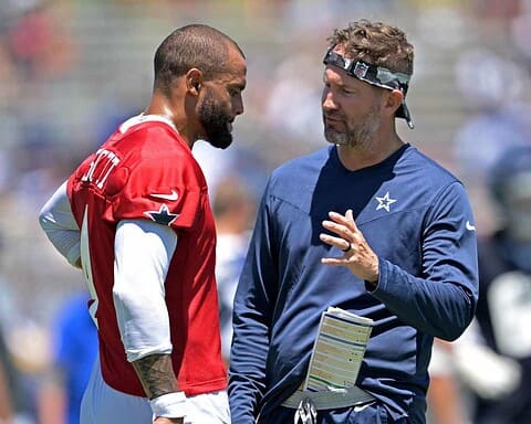 Wide receiver on football field talking with coach, discussing game strategy during NFL practice, Dallas Cowboys player and staff, sunny day, team dynamics, inside the star complex, professional football, sports leadership.