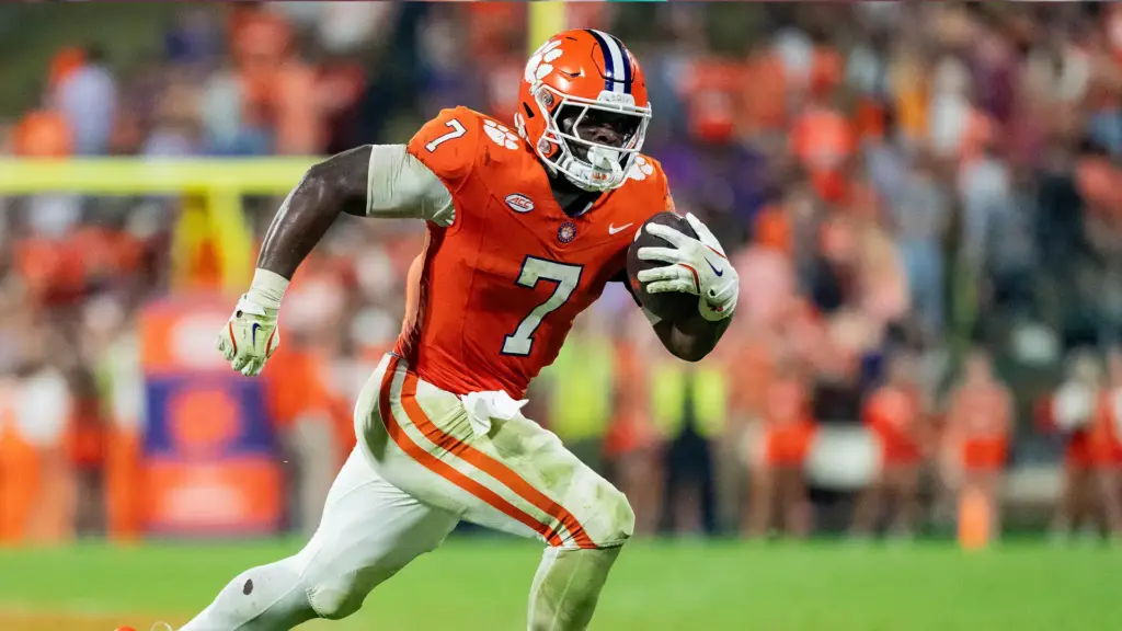 Running football player wearing orange and white uniform holding a football during game.