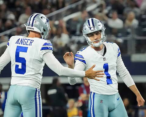 Dallas Cowboys football players celebrating on the field during a game, wearing white jerseys with blue numbering, in front of a stadium crowd.