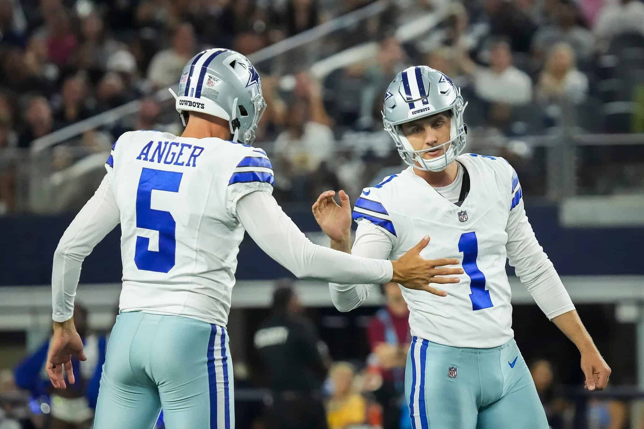 Dallas Cowboys football players celebrating on the field during a game, wearing white jerseys with blue numbering, in front of a stadium crowd.