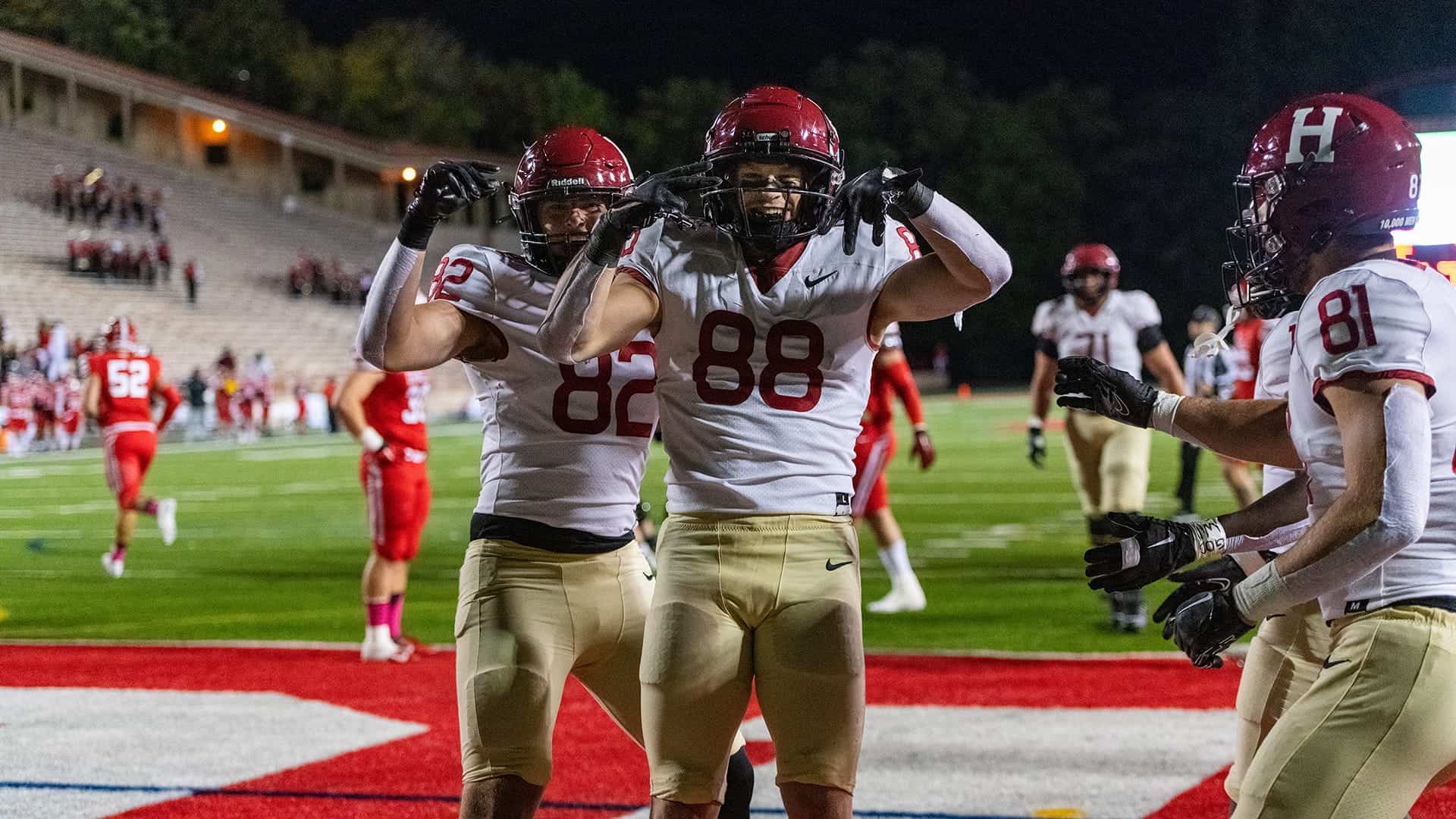 Celebrating a football touchdown at night with players in white and red uniforms, showcasing team spirit, athletic performance, and excitement on the field.