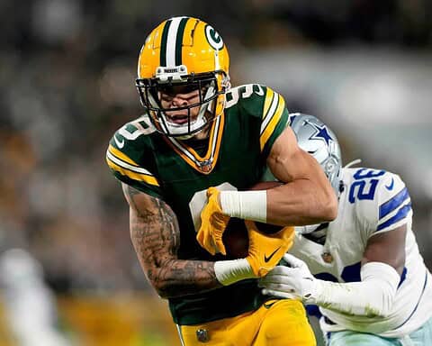 Green Bay Packers player running with football during game against Dallas Cowboys, defensive player attempting to tackle, NFL football action, inside football stadium, team uniforms.